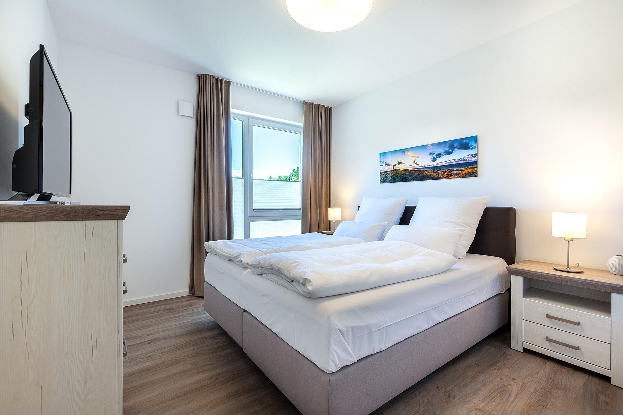 Habitación de hotel con una cama, una mesita de noche, una lámpara, un cuadro y vistas al exterior.