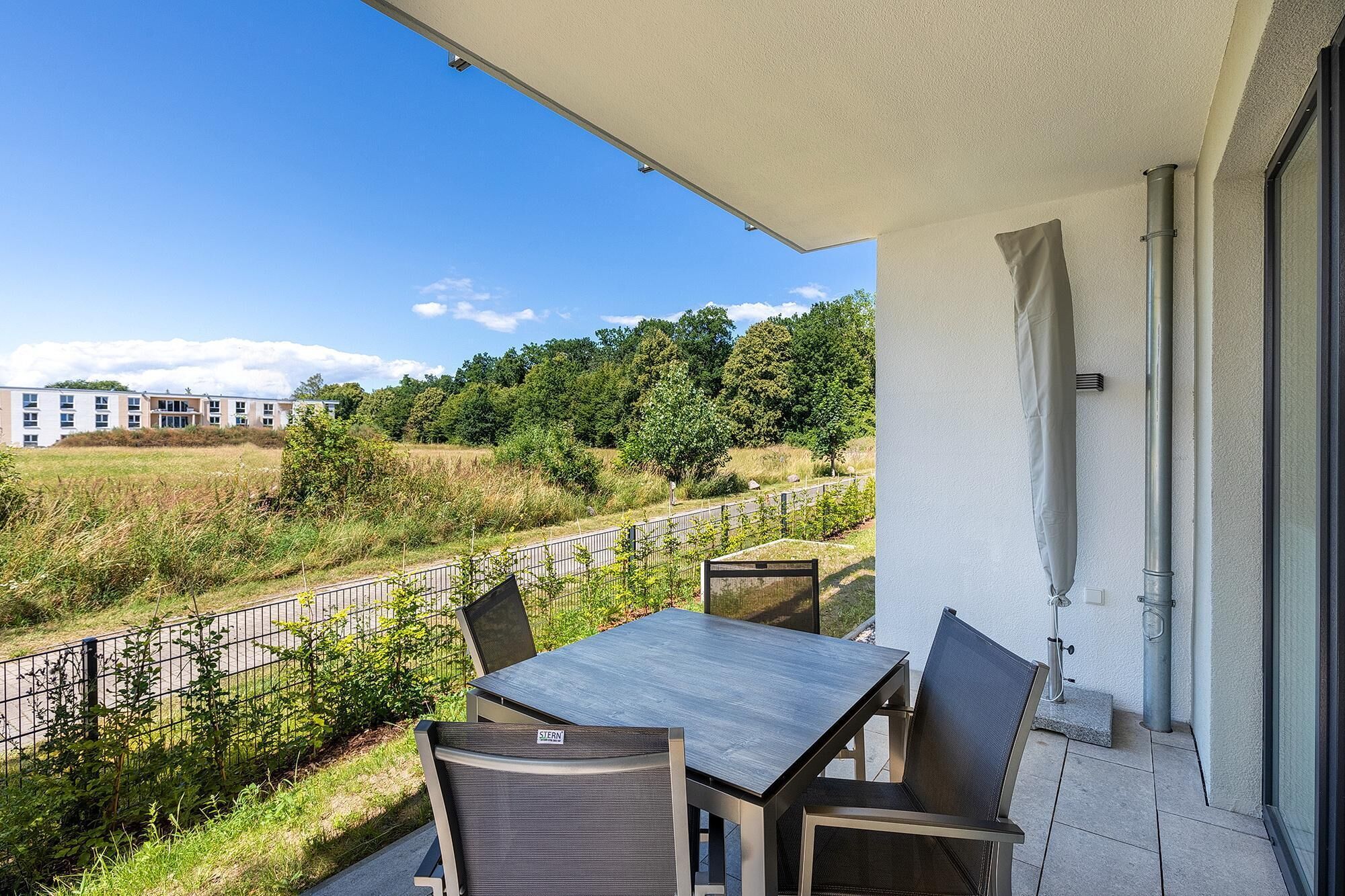 A balcony with a table and chairs, overlooking a grassy area and a building in the distance.