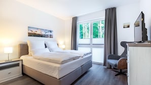 A modern hotel room with a large bed, a desk, a chair, and a window with curtains.