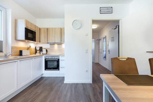 Una cocina moderna con armarios blancos, horno empotrado y microondas. Hay una mesa de comedor de madera con sillas.