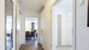 A hotel hallway with a wooden floor, a dining area with chairs and a table, and a glass shower area.