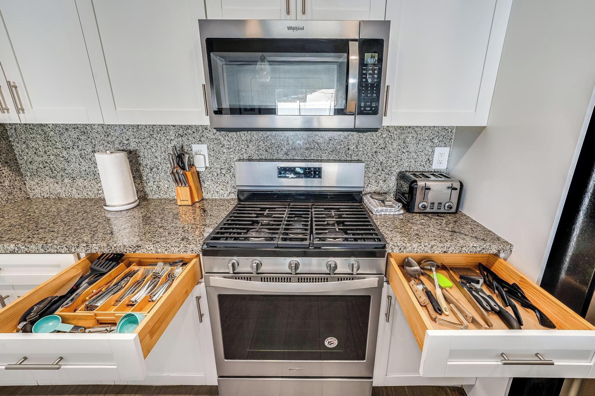 Una cocina equipada con microondas, tostadora, estufa y horno. Hay cajones con utensilios de cocina.