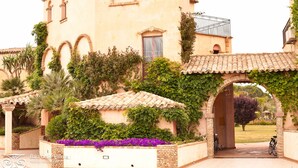 A building with arched windows and a tiled roof, surrounded by greenery and a paved pathway. - Residence Baia delle Palme (Pula)