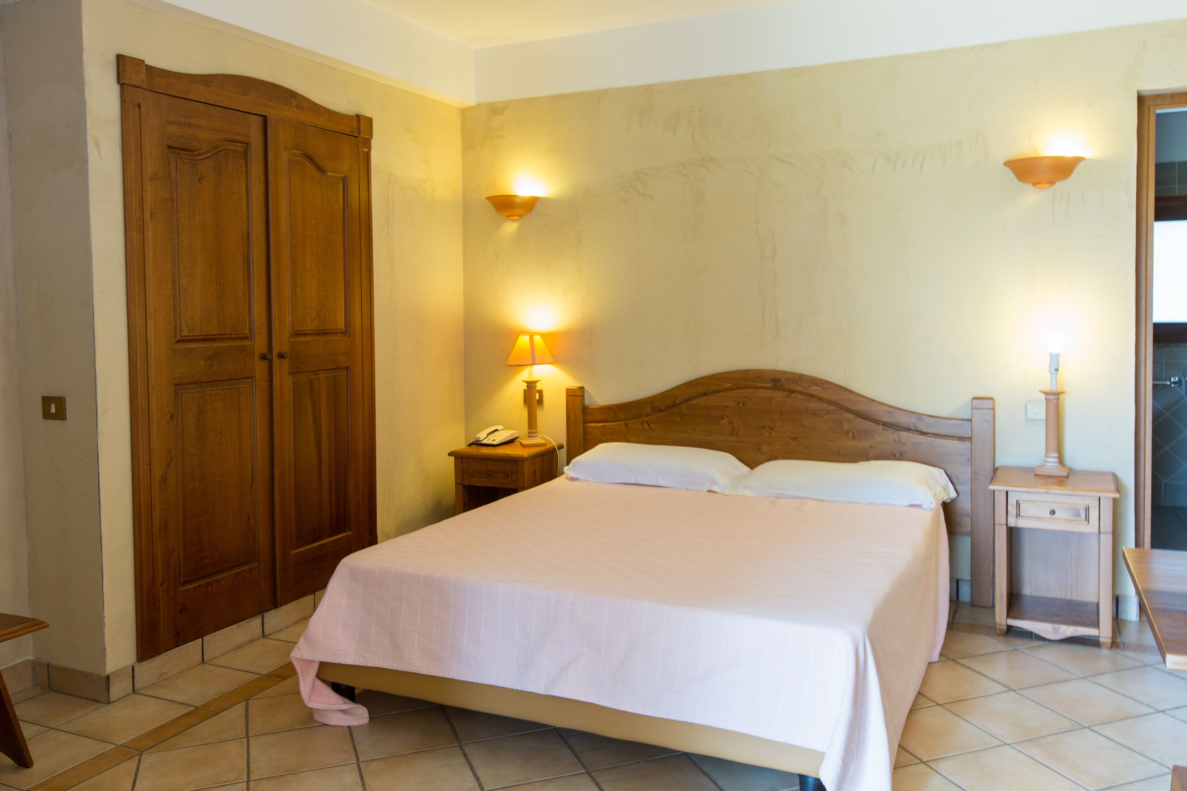 A bedroom with a bed, wooden wardrobe, bedside lamps, and a nightstand.