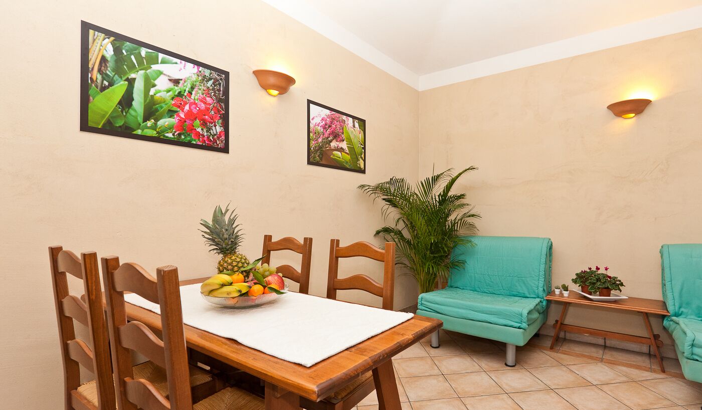 Un comedor con una mesa y sillas de madera, un sofá color turquesa y dos lámparas fijadas a la pared.