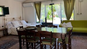 Um quarto com cama, mesa de jantar com cadeiras, sofá e janelas amplas com cortinas.