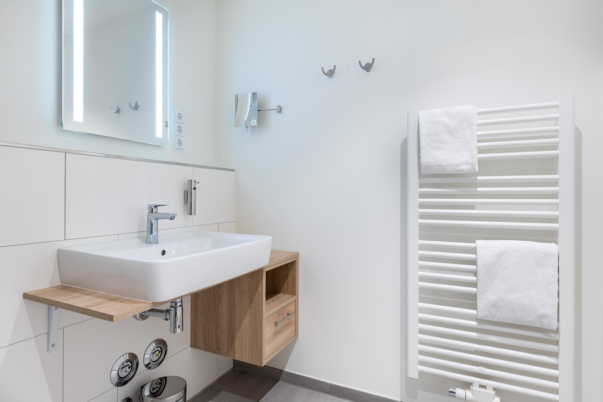 Une salle de bain moderne avec un lavabo blanc, un meuble-lavabo en bois et un porte-serviettes avec des serviettes.