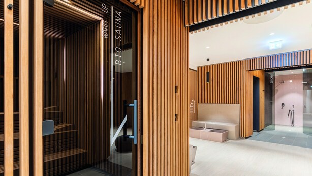 Un moderno espacio de spa con paneles de madera, un mostrador de recepción y una zona de duchas visible.