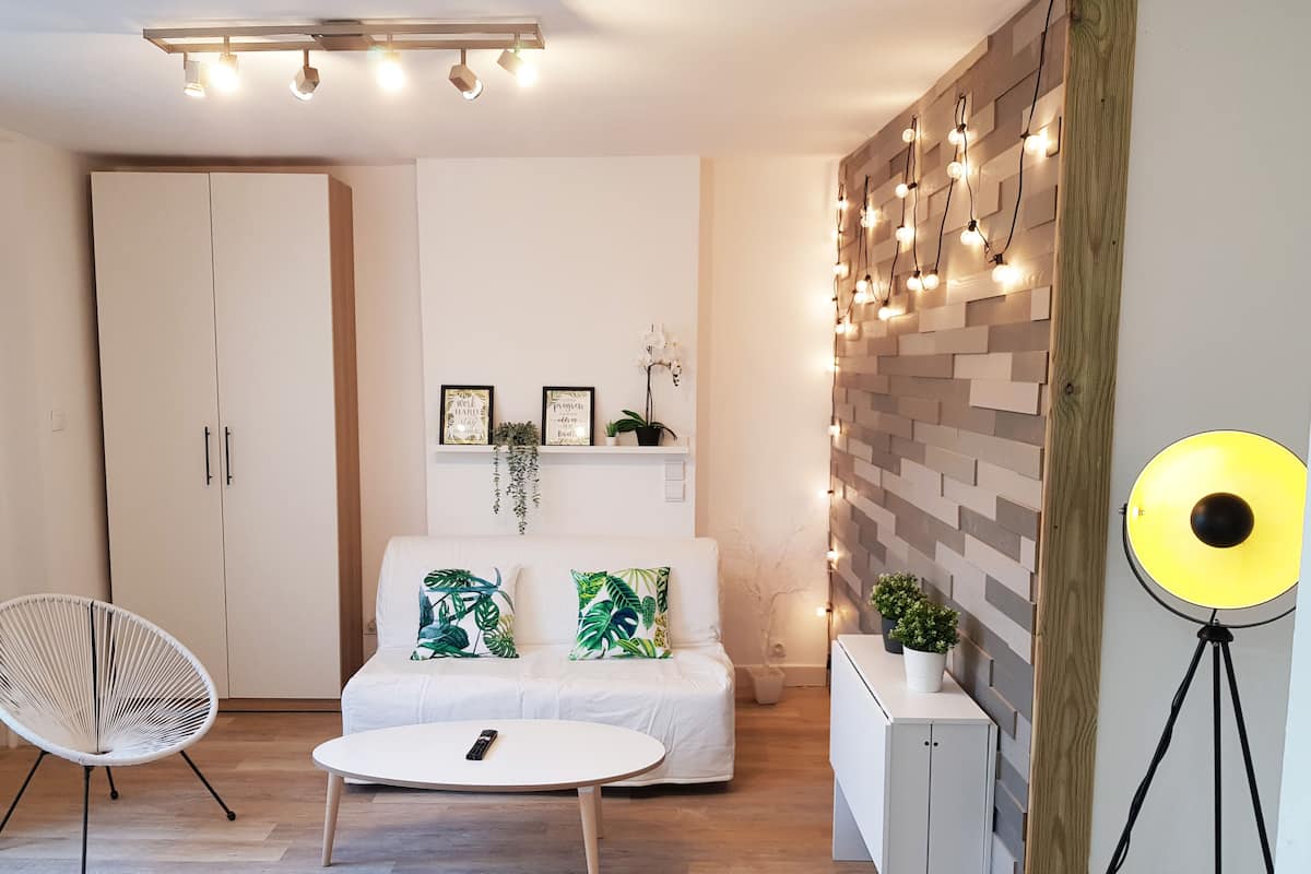 Un salon moderne avec un canapé blanc, une table basse ronde, une chaise blanche et un luminaire fixé au mur.