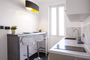 A modern kitchen with a built-in island, two bar stools, a pendant light, a window, and a stainless steel sink.