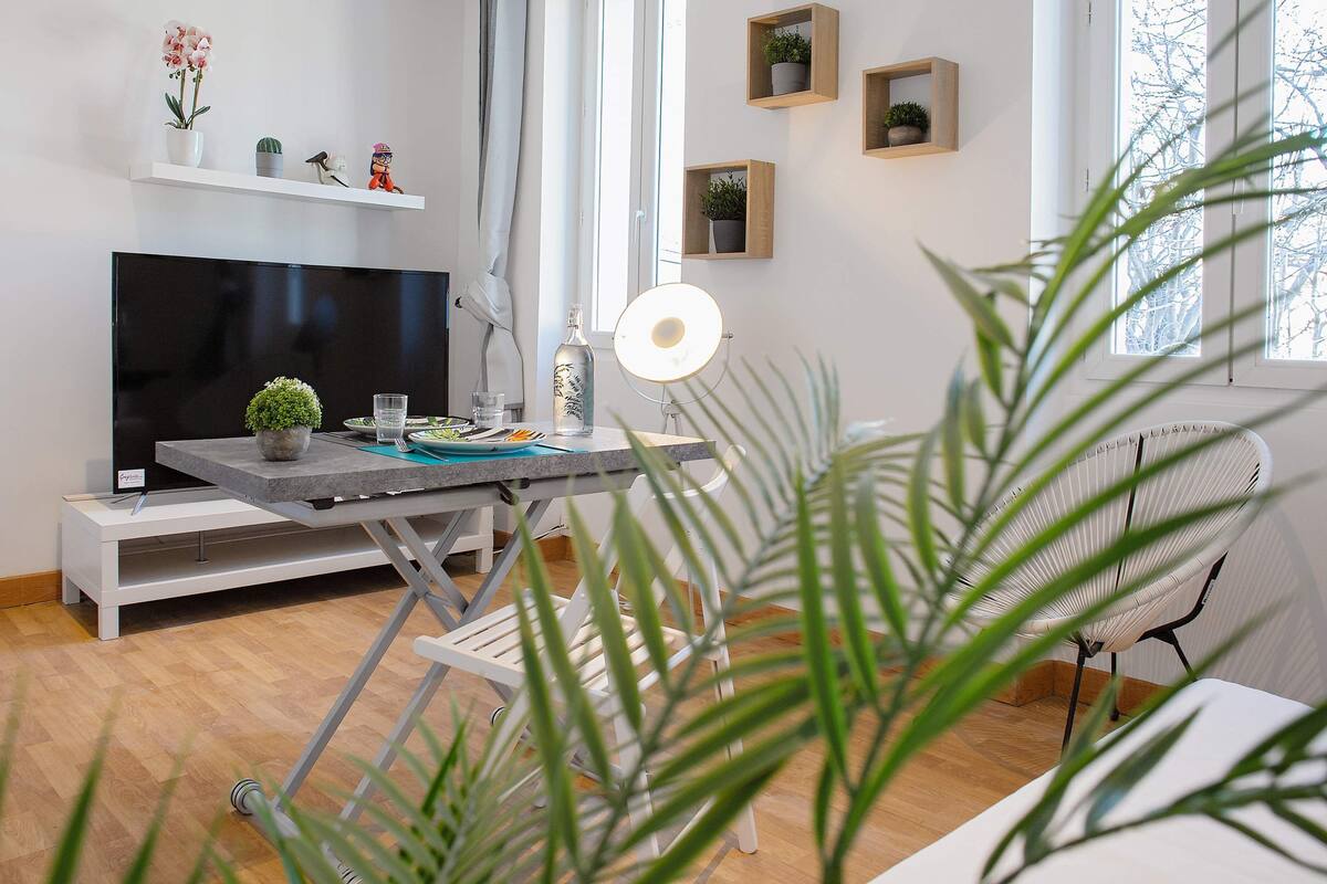 Un salon moderne doté d’un téléviseur à écran plat, d’une table à manger avec des chaises, d’un lampadaire et de divers objets décoratifs disposés sur des étagères.