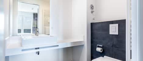 Un baño moderno con un tocador blanco, un espejo grande, un inodoro y una zona de ducha.