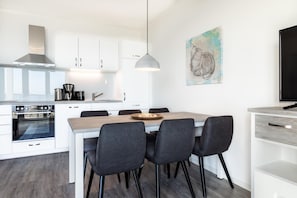 Una cocina moderna con armarios blancos, horno empotrado y comedor con mesa de madera y cuatro sillas.