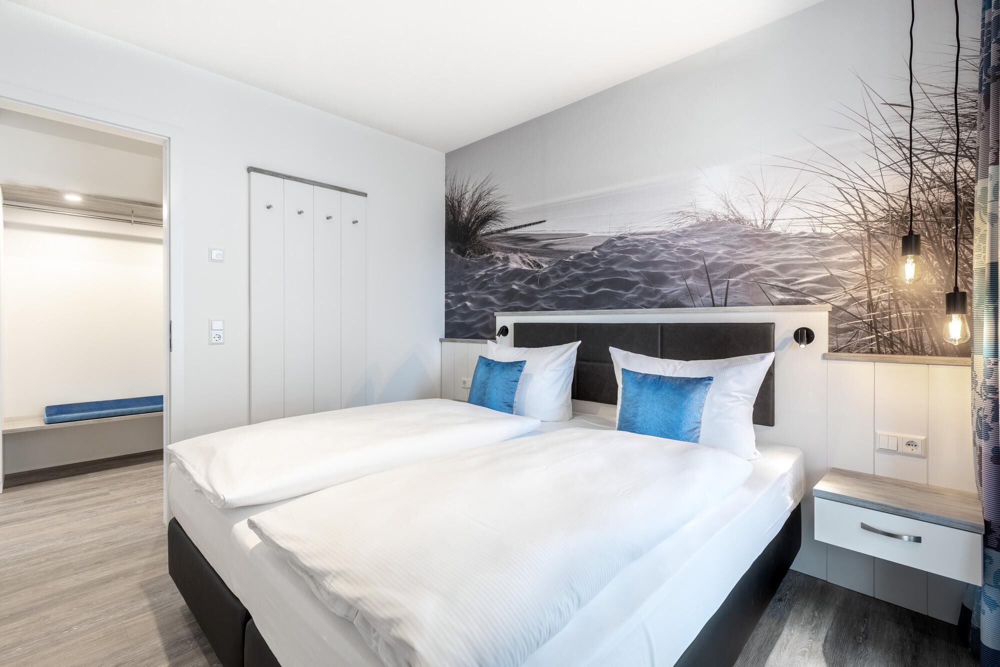 A modern bedroom with a large bed, a headboard, a nightstand, a wall-mounted shelf, and a wardrobe.