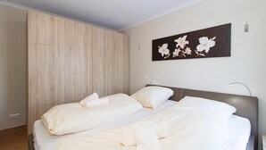 A bedroom with two beds, a wooden wardrobe, and a wall-mounted floral artwork.