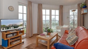 A living room with a television, a coffee table, a sofa, and a window with curtains.