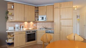 A compact kitchen with wooden cabinets, a microwave, a stove, and a sink. There is a dining table with two chairs.
