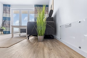 A room with a grey sofa, a potted plant, a small table, and a sign reading 'Hundeplatz'. - Familien-apartment mit Balkon und Einmalig-schönem Meerblick in der Ersten Reihe (Ostseeheilbad Großenbrode)