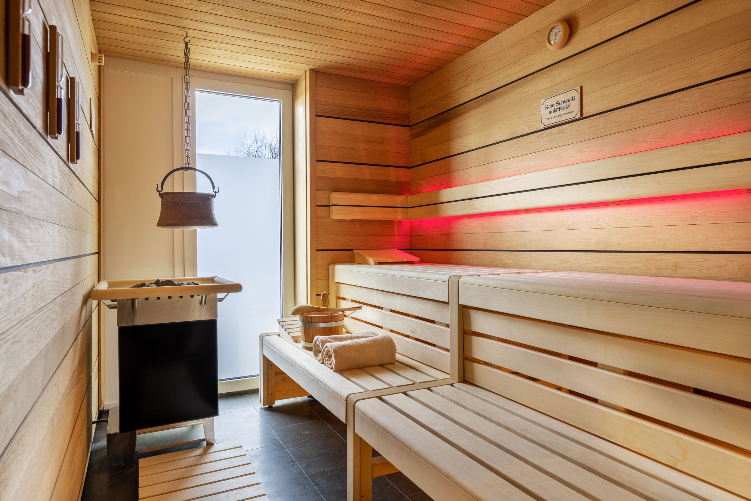 Una sauna con panche in legno, una panca con asciugamani, un catino e un bollitore appeso.