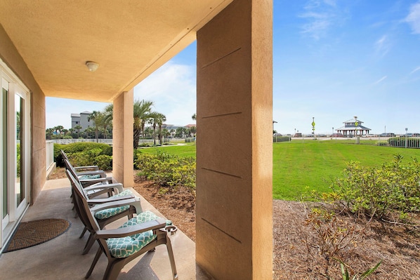 A covered outdoor seating area with chairs and a view of a grassy field and distant buildings.