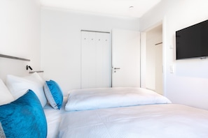 A bedroom with a bed, pillows, a wardrobe, and a TV mounted on the wall.