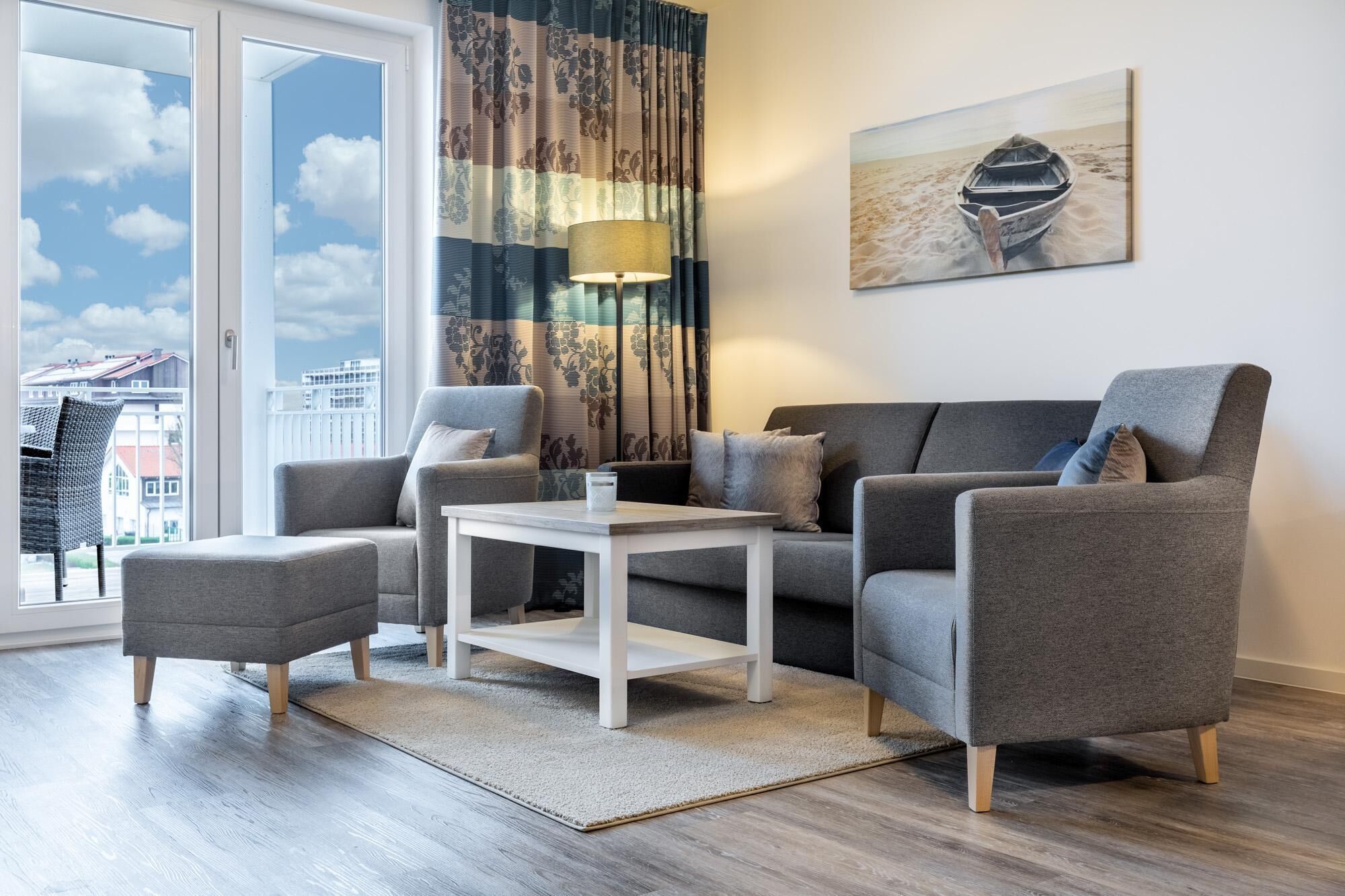 Ein modernes Wohnzimmer mit grauem Sofa, Sesseln, einem Couchtisch und Blick auf Gebäude durch große Fenster.