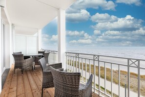 A balcony with wicker furniture overlooking a beach.