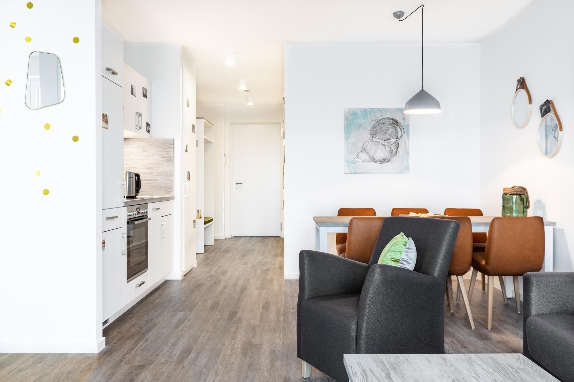 A modern kitchen with white cabinets, a built-in oven, and a dining area with a table and chairs.