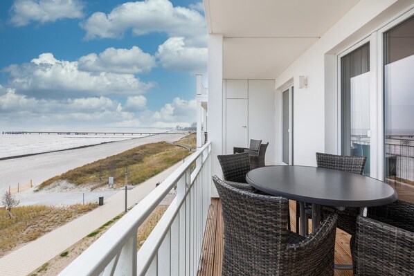 A balcony with wicker furniture and a view of a beach and a bridge.