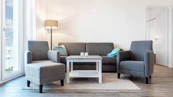 Ein modernes Wohnzimmer mit einem grauen Sofa, zwei Sesseln, einem kleinen weißen Couchtisch und einer Stehlampe.