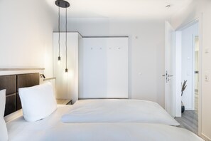 A modern hotel room with a large bed, a bedside table, a wardrobe, and a door leading to another room. - Traumhaft-schön Gelegenes Apartment in Erster Reihe am Strand mit Meerblick (Ostseeheilbad Großenbrode)