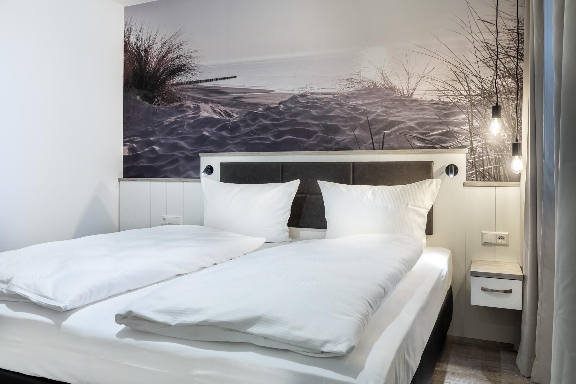 Ein modernes Schlafzimmer mit einem Bett, einem Nachttisch und einer Wandmalerei, die eine Strandansicht zeigt.