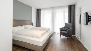 Une chambre d’hôtel moderne, dotée d’un grand lit, d’une chaise, d’un téléviseur et d’une fenêtre avec des rideaux.