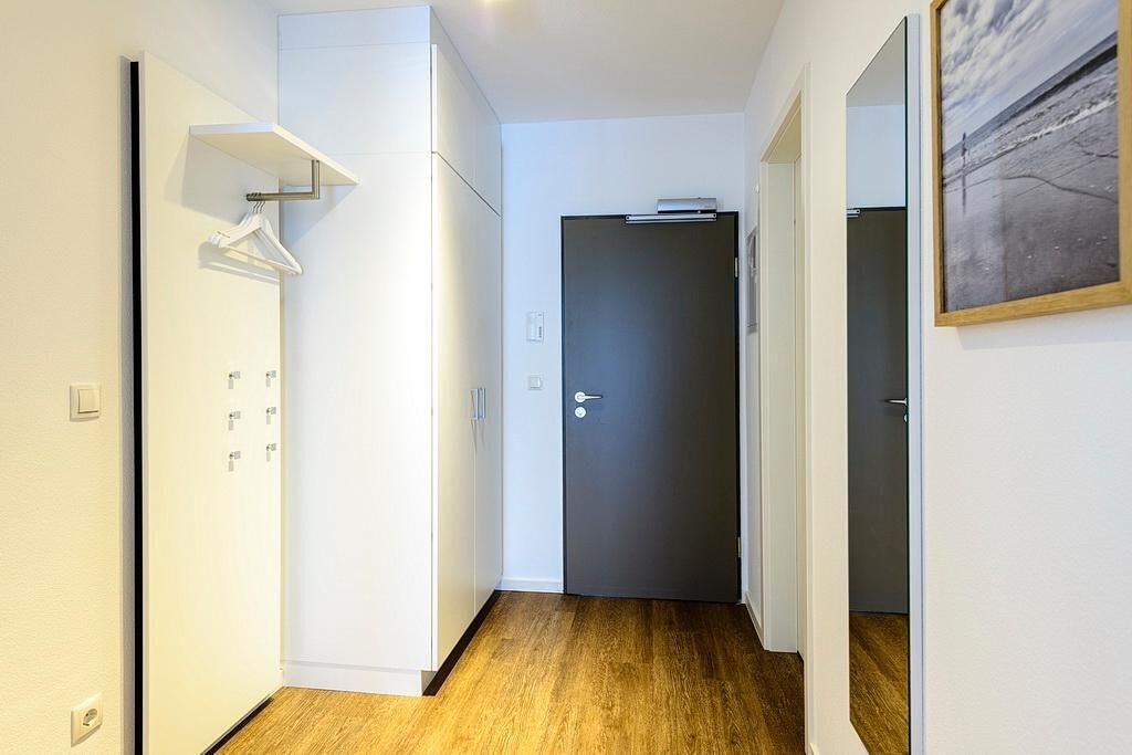 Ein Flur mit Holzboden, einem weißen Kleiderschrank, einer dunklen Tür und einem Gemälde an der Wand.
