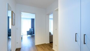 Un couloir moderne avec un plancher en bois, des murs blancs et une vue sur un espace de vie comprenant un canapé et des rideaux.