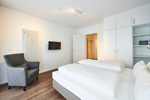 Una habitación de hotel con cama, una silla, un televisor y un armario.
