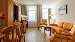 Ein Wohnzimmer mit einem Holzschrank, einem Fernseher, einem blumigen Sessel, einem Sofa und einer Lampe.