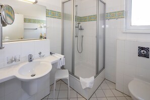 Ett badrum med en dusch som är avskärmad med glasväggar, ett handfat och en toalett.