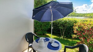 Ein runder Tisch mit weißer Tischdecke, zwei Stühle, einem blauen Sonnenschirm und einem weißen Teekännchen darauf.