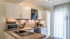 Une cuisine moderne avec des armoires blanches, un plan de travail en bois, un four encastré et une machine à café.