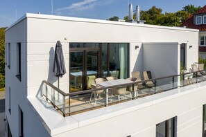 Un edificio moderno con balcón de cristal, mobiliario exterior y vistas despejadas del entorno.