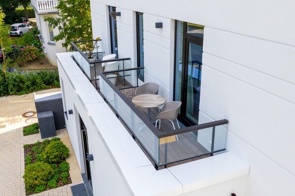 Un edificio moderno con un balcón de cristal y mobiliario para disfrutar al aire libre.