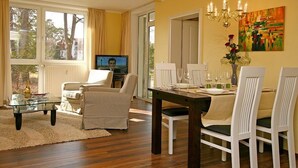 Una sala de estar con televisor, un comedor con una mesa lista para cuatro personas y un ventanal con cortinas.
