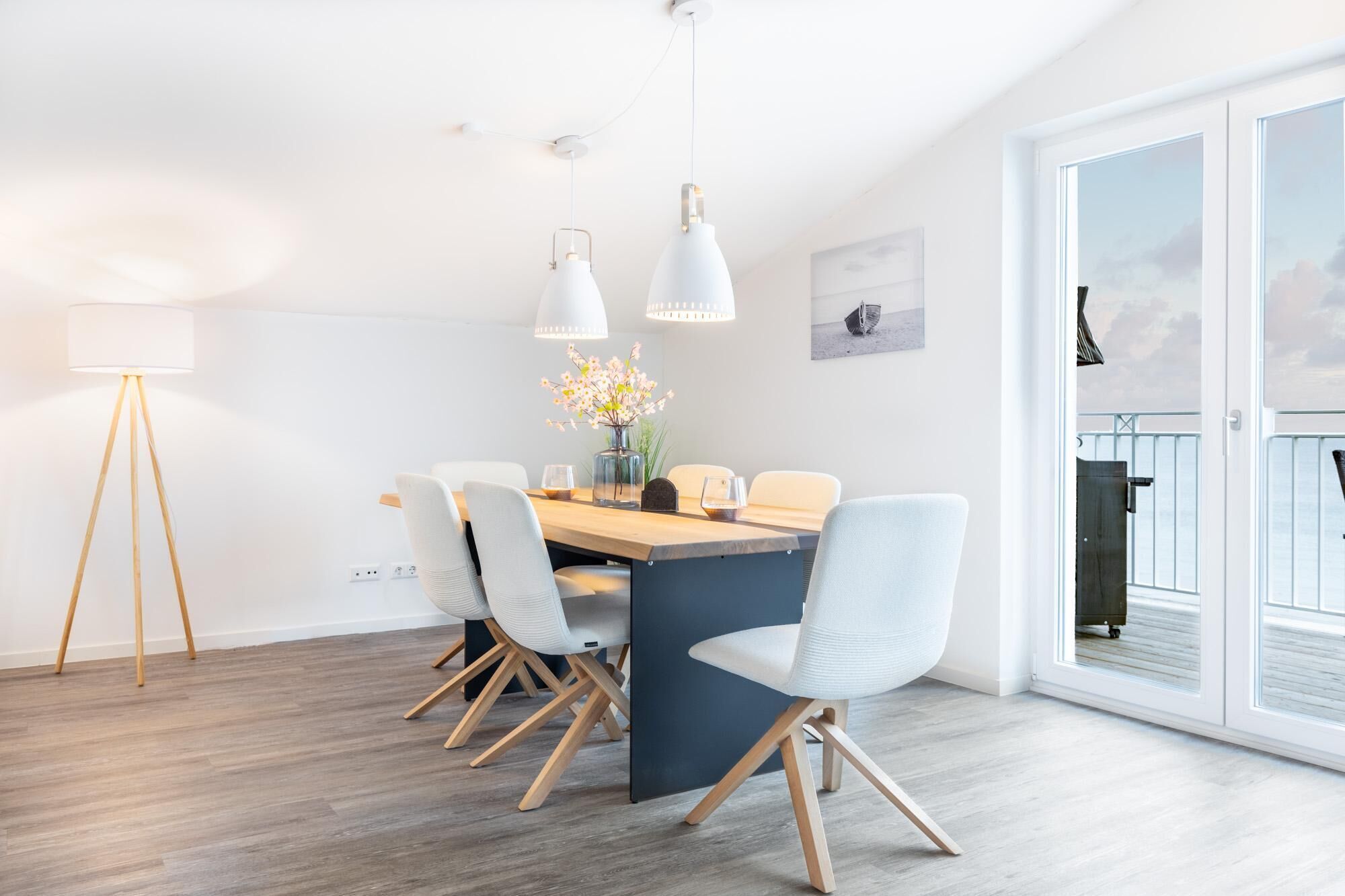 Et moderne spiseområde med et træbord, hvide stole og hængende lamper.