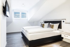A modern bedroom with a black headboard, a large window, and a wooden floor.