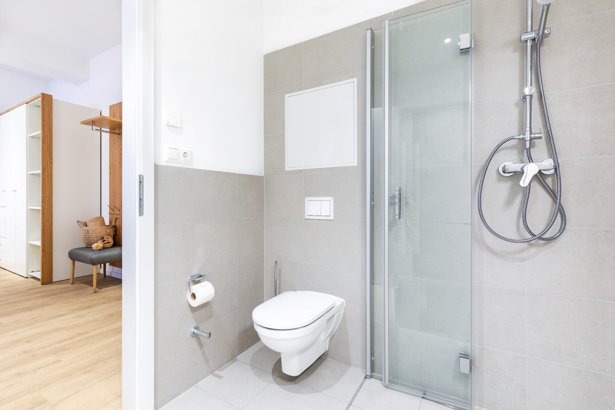 A modern bathroom with a glass shower enclosure, a toilet, and a wooden vanity with a basket.