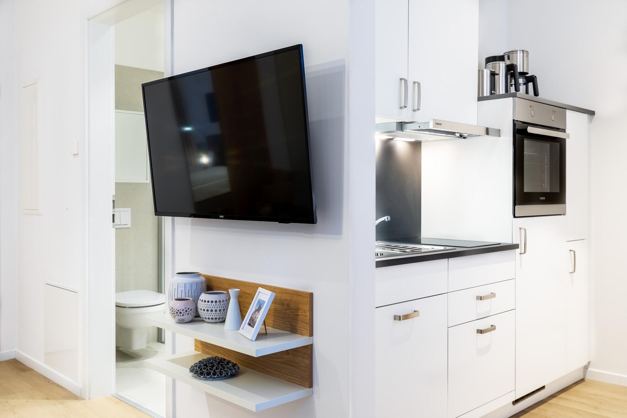 A modern kitchen with a flat-screen TV, built-in oven, and coffee maker.