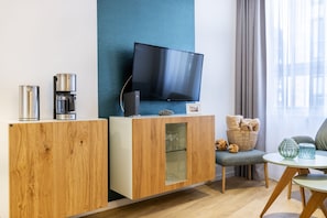 Un salon moderne avec un meuble en bois, une machine à café, un téléviseur à écran plat, un panier en osier et une petite table ronde.