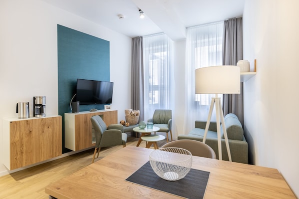 Un salon moderne avec un téléviseur à écran plat, des meubles en bois, une table à manger avec un saladier blanc et une lampe.