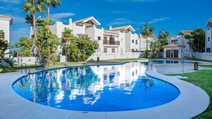 A swimming pool surrounded by white buildings with balconies, palm trees, and a clear blue sky. - Alcaidesa Golf and Beach 2356 (La Alcaidesa)